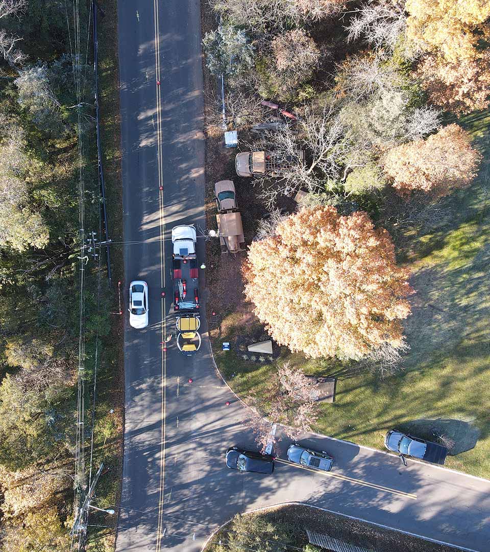 Aerial view of a roadside utility or maintenance operation on a two-lane road surrounded by autumn trees