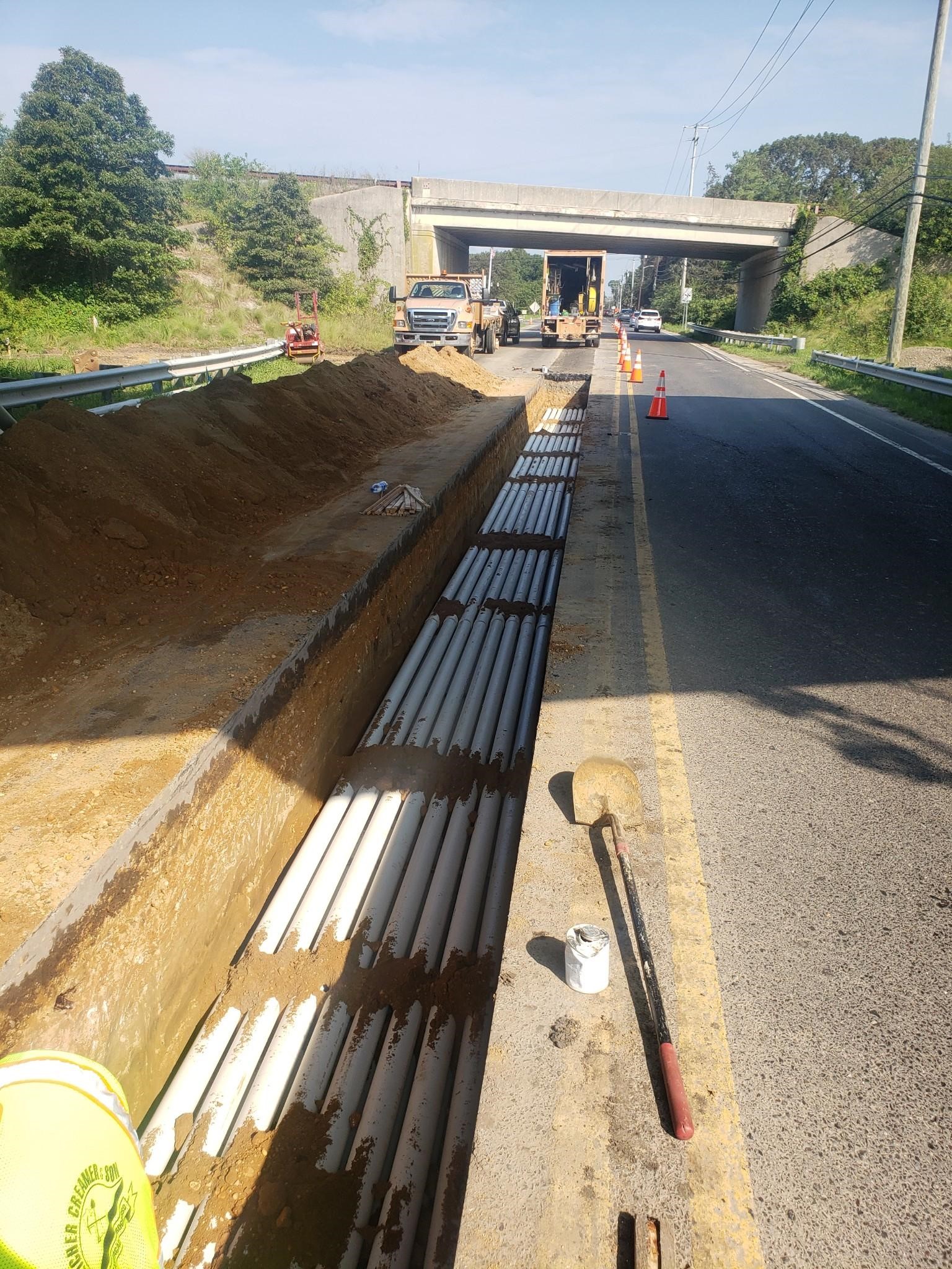 A trench is being dug alongside a roadway for the installation of multiple underground utility conduit