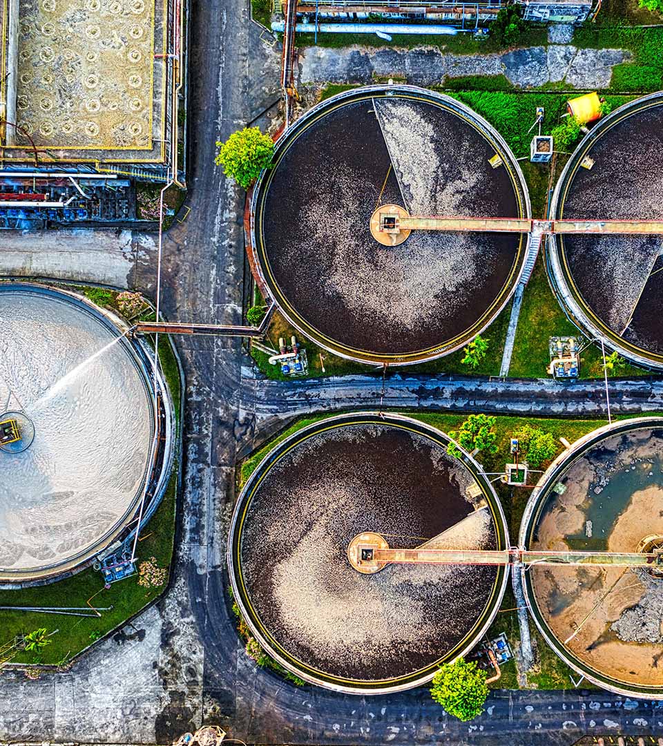 A vibrant aerial view of a wastewater treatment plant featuring several large circular clarifier tanks in various stages of operation.